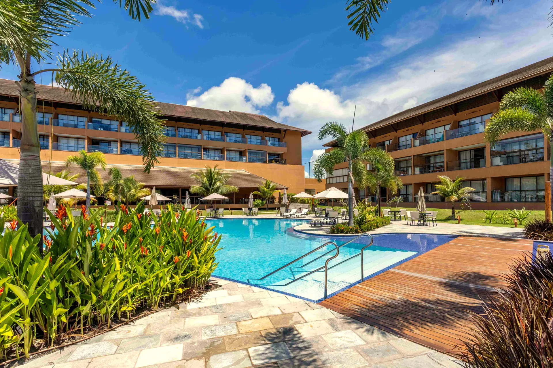 Piscina do Eco Resort Praia dos Carneiros com deck de madeira, jardins tropicais e os prédios ao fundo