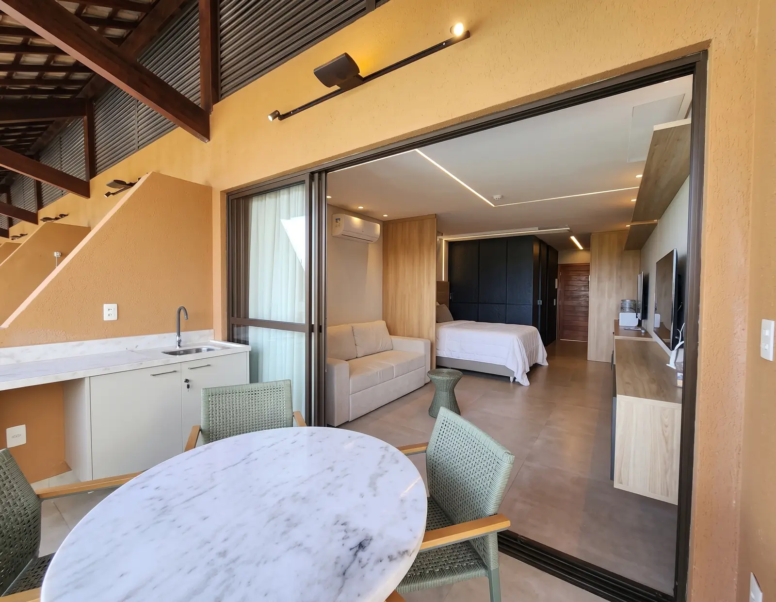 Suíte com cama de casal e sofá vista da varanda com mesa de mármore